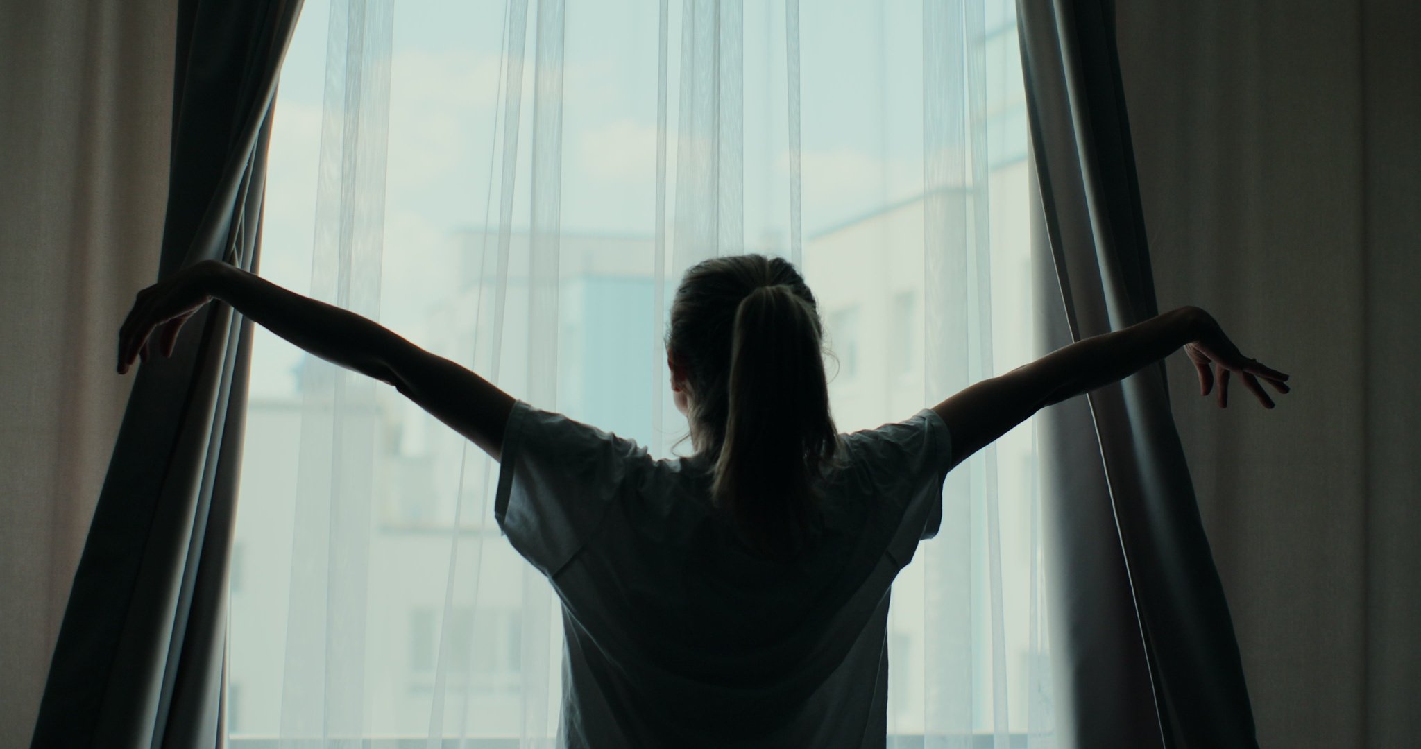 Young attractive woman approaches a window, and opens curtai